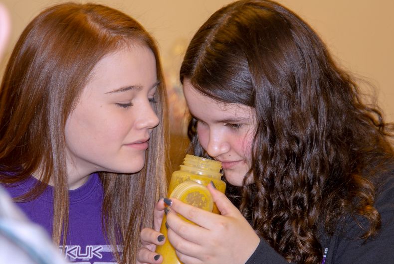 A group of kids smelling a bottle of something.