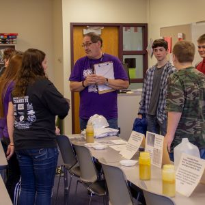 thumbnail image of Kids gathered around a table with informational objects and papers.