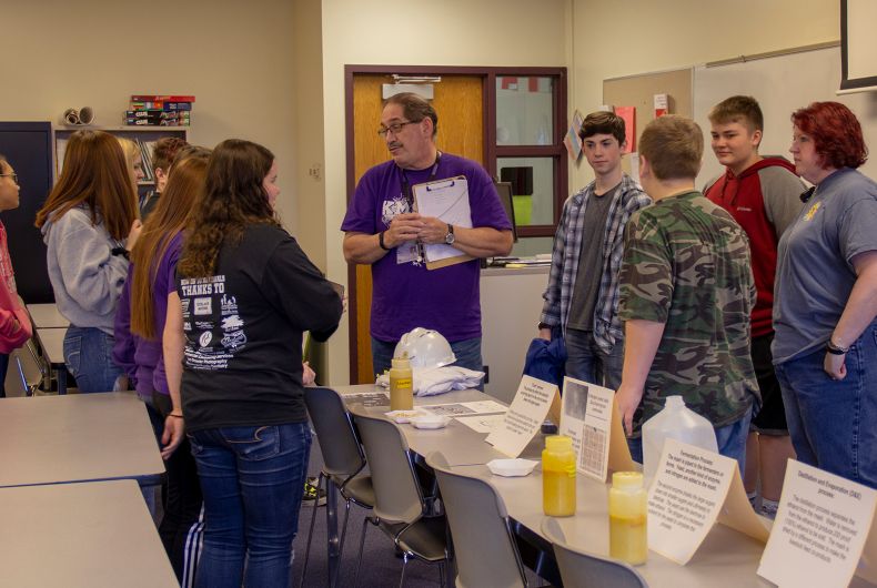 Kids gathered around a table with informational objects and papers.
