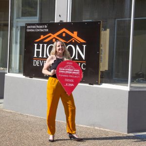 thumbnail image of A woman standing outside a storefront holding a sign
